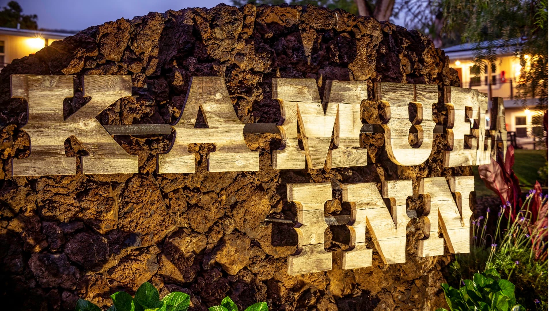 Wooden sign displaying "Kamuela Inn" against a rocky background.