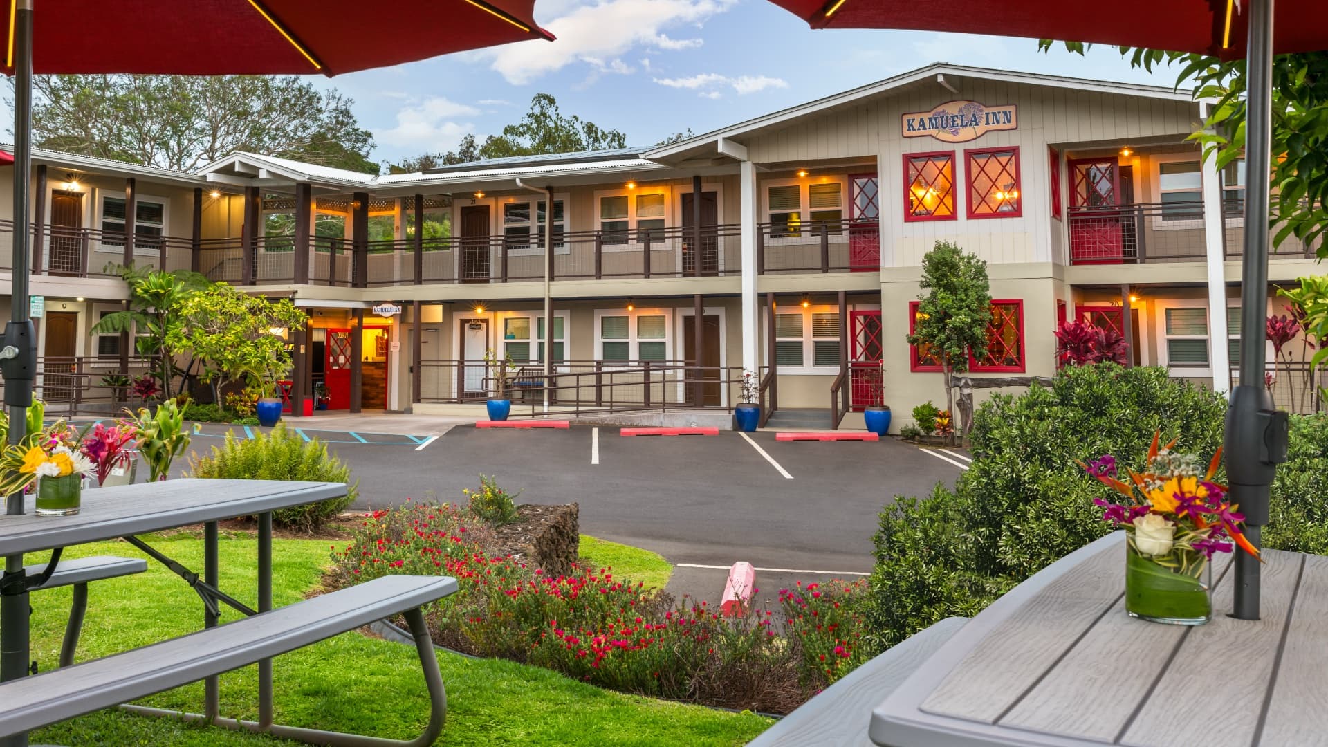 A colorful inn surrounded by greenery and vibrant flowers, featuring outdoor seating and a welcoming entrance.